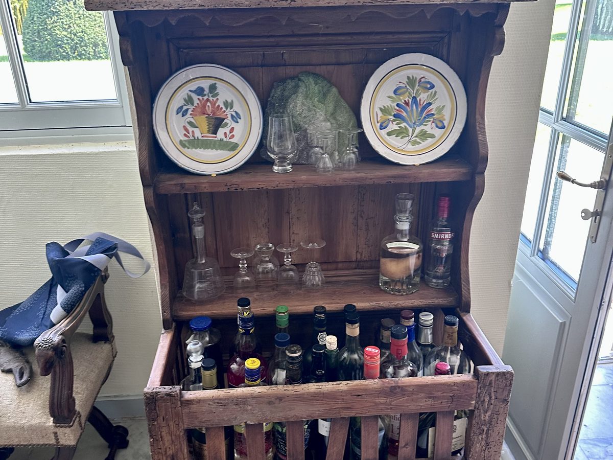 An old French wooden buffet with faience plates, glassware, and bottles.