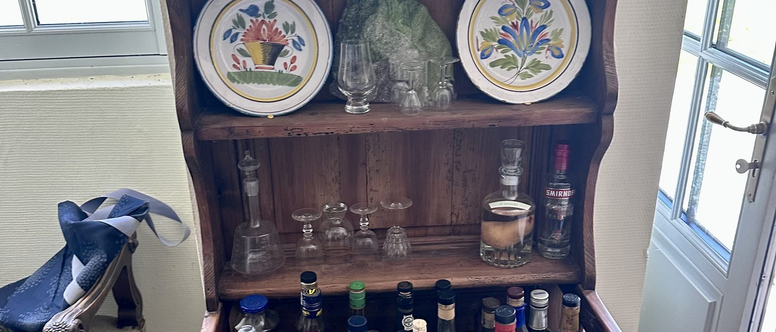An old French wooden buffet at Manoir du Suquet, with hand-painted faience plates, antique glassware, and bottles — the kind of honest, collected object the post discusses.