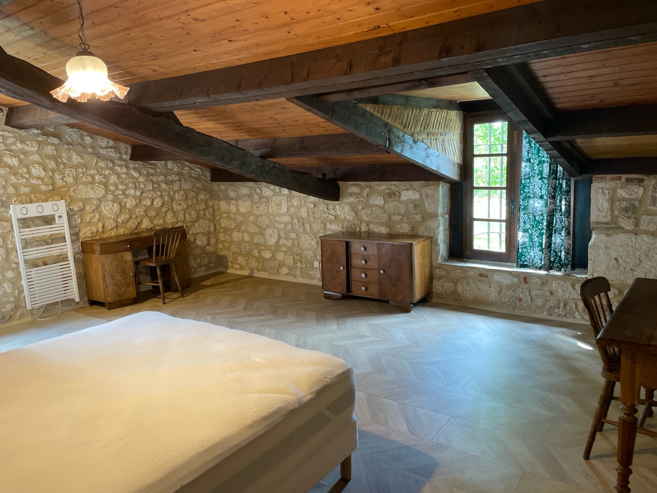 Bedroom one at Maison des Artistes, a long stone-walled room under exposed roof timbers