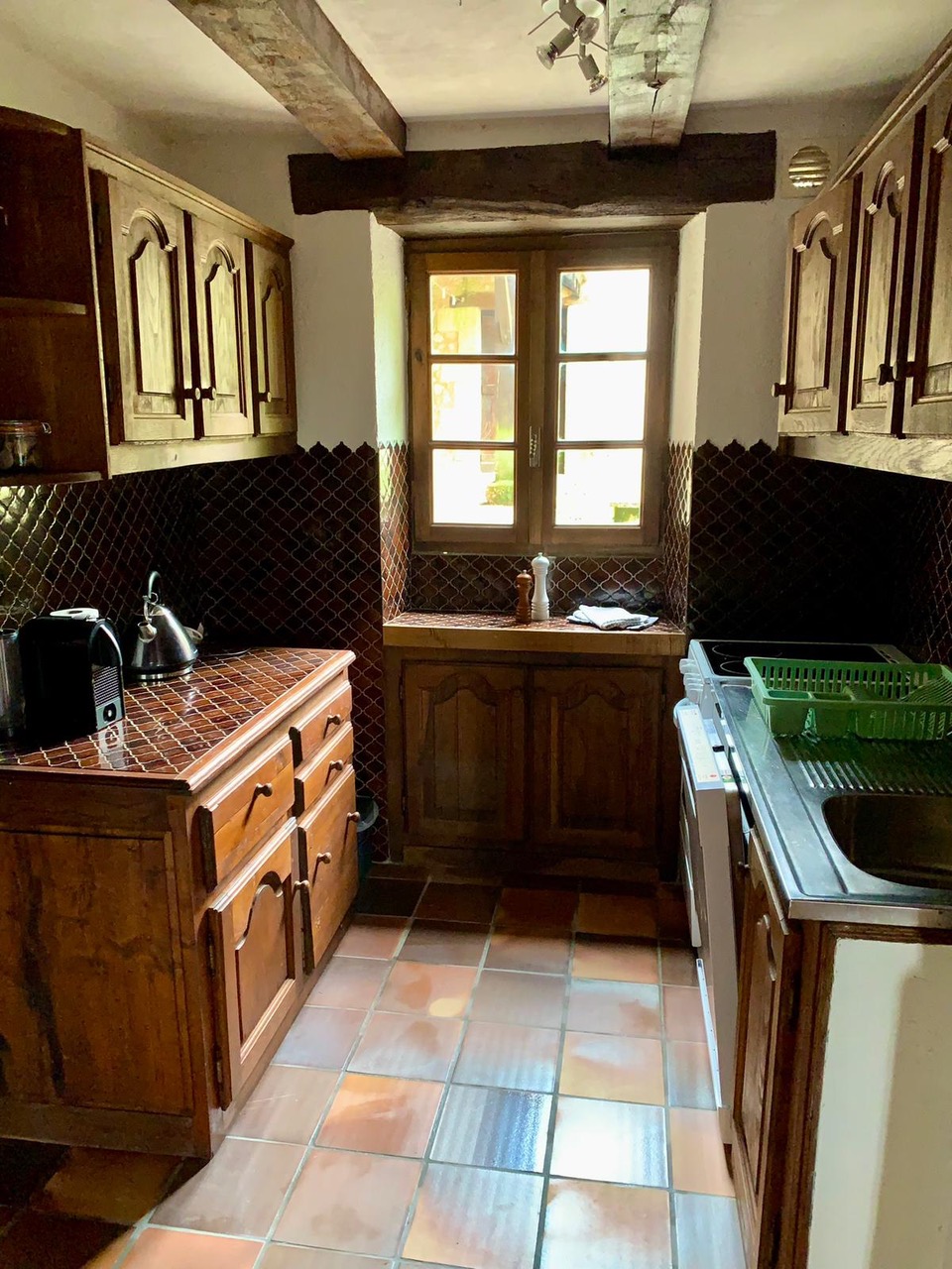 The galley kitchen at Maison des Artistes, with dark zellige tiling and a window onto the grounds