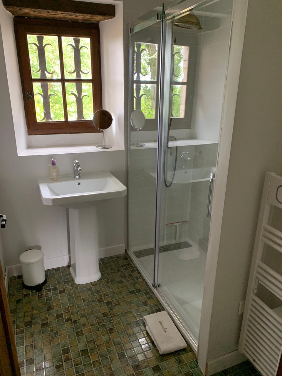 The shower room at Maison des Artistes, with a green mosaic floor and a window over the grounds