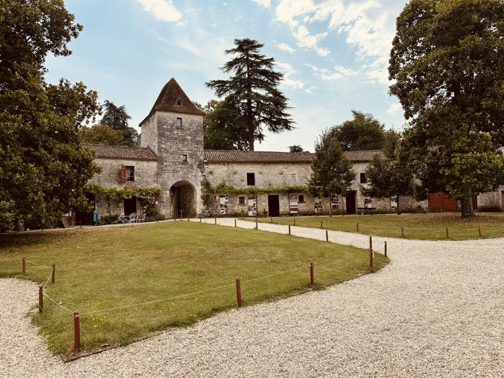 The Bridoire courtyard with the central pigeonnier tower, the wisteria-clad outbuildings on either side, the cedar tree above, and the gravel path approaching from the foreground
