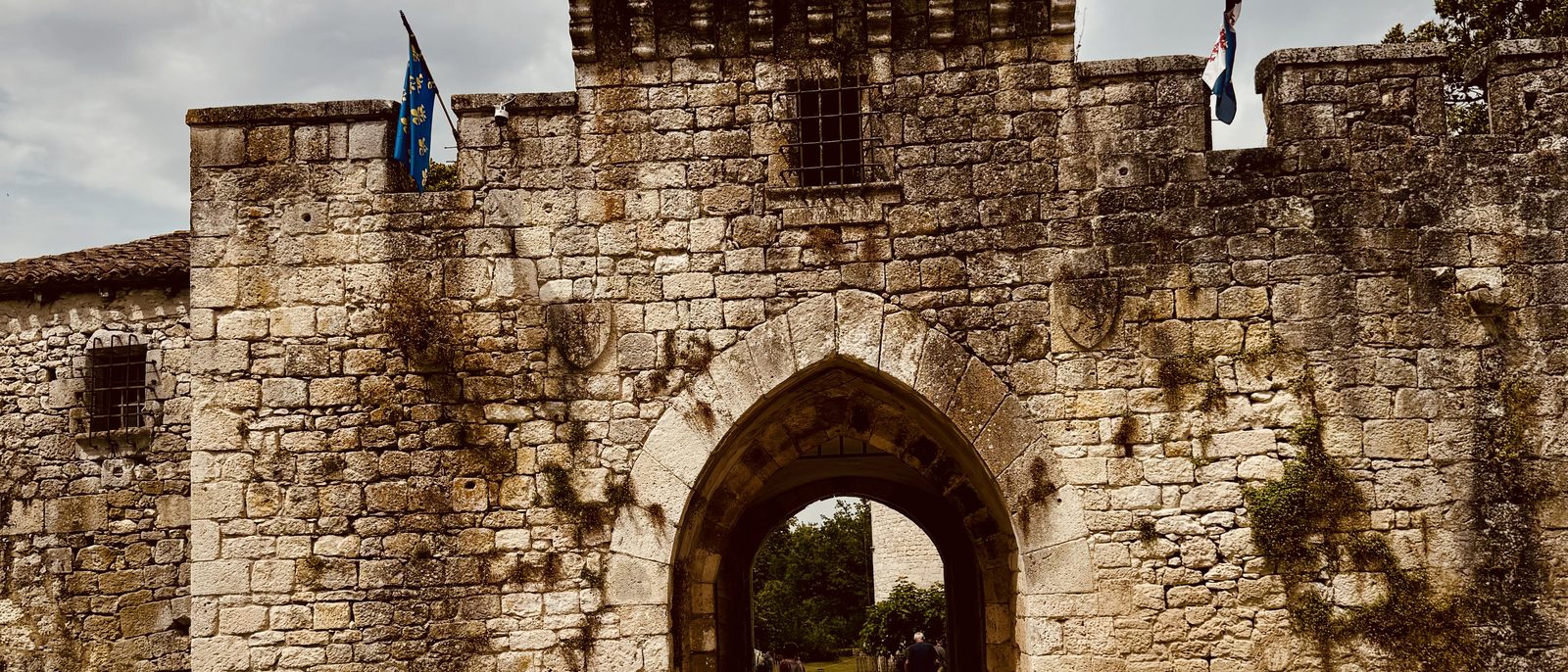 The fortified gateway of Château de Bridoire — stone arch, flags, ramparts, glimpse of the courtyard beyond.