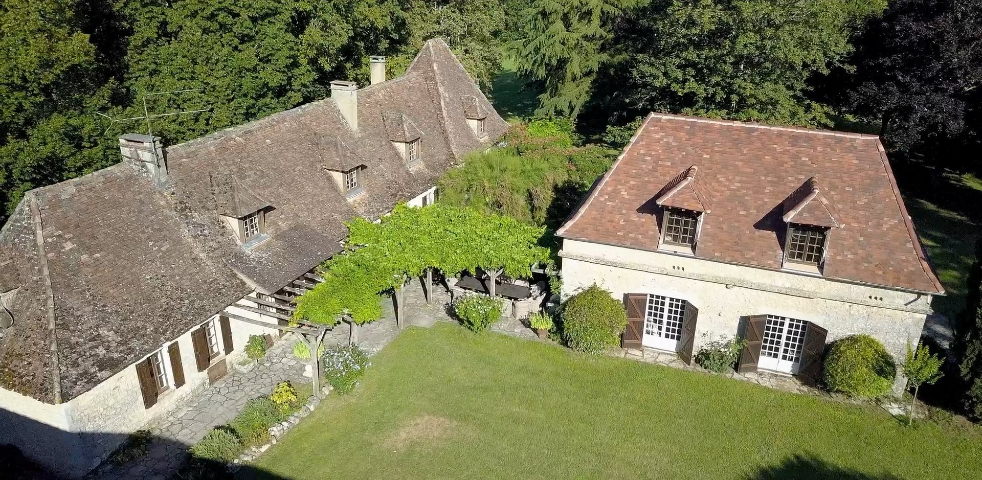 Aerial view of the courtyard at Manoir du Suquet — the vine-covered pergola, the long table and the lawn