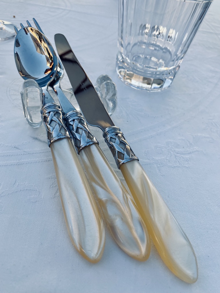 Mother-of-pearl handled cutlery at La Chartreuse du Bignac on damask linen with crystal rests and a faceted tumbler.