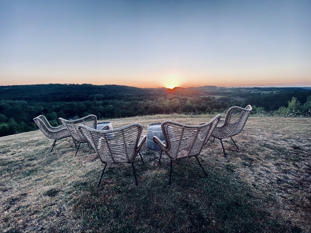 Wicker armchairs in a half-circle around a wine-barrel table at sunset on the hill at Bignac, the Dordogne forest fading into the horizon.