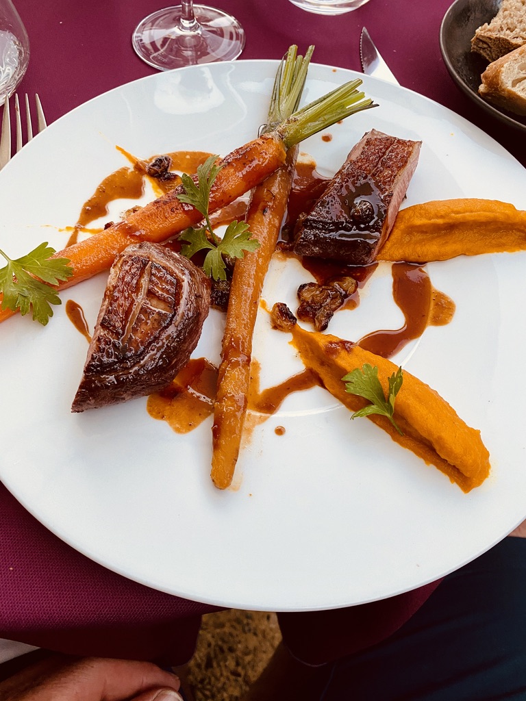 A duck breast at L'Atelier with glazed baby carrots — the carrot tops still attached — sweet potato purée, glossy reduction sauce.