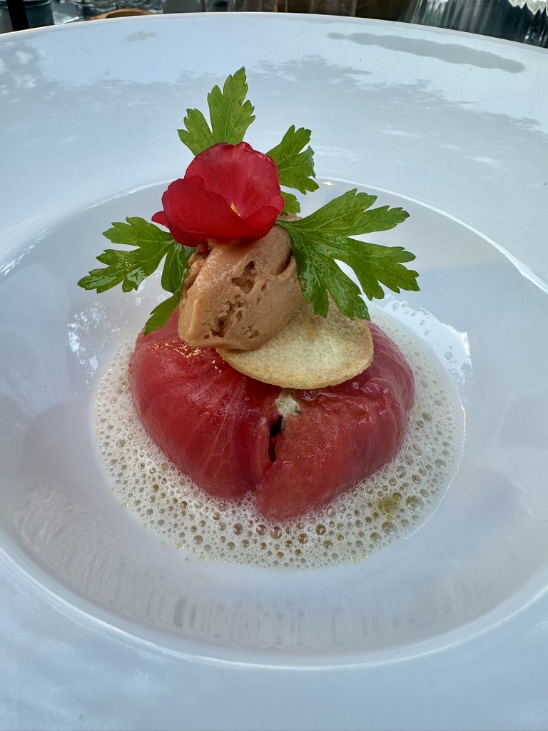 A stuffed tomato at L'Atelier — chicken liver mousse quenelle, parsley, edible red flower, on a foamed bouillon.