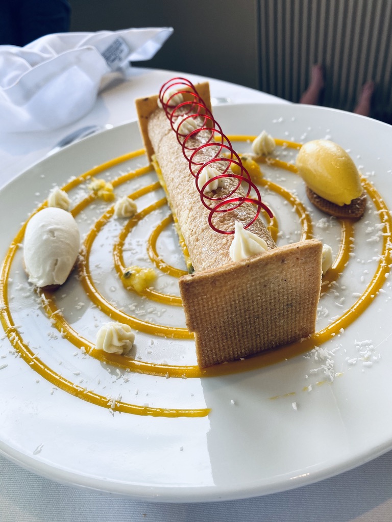 A dessert at La Tour des Vents — cylindrical biscuit, red sugar spiral, passion fruit coulis circles, sorbet quenelle.