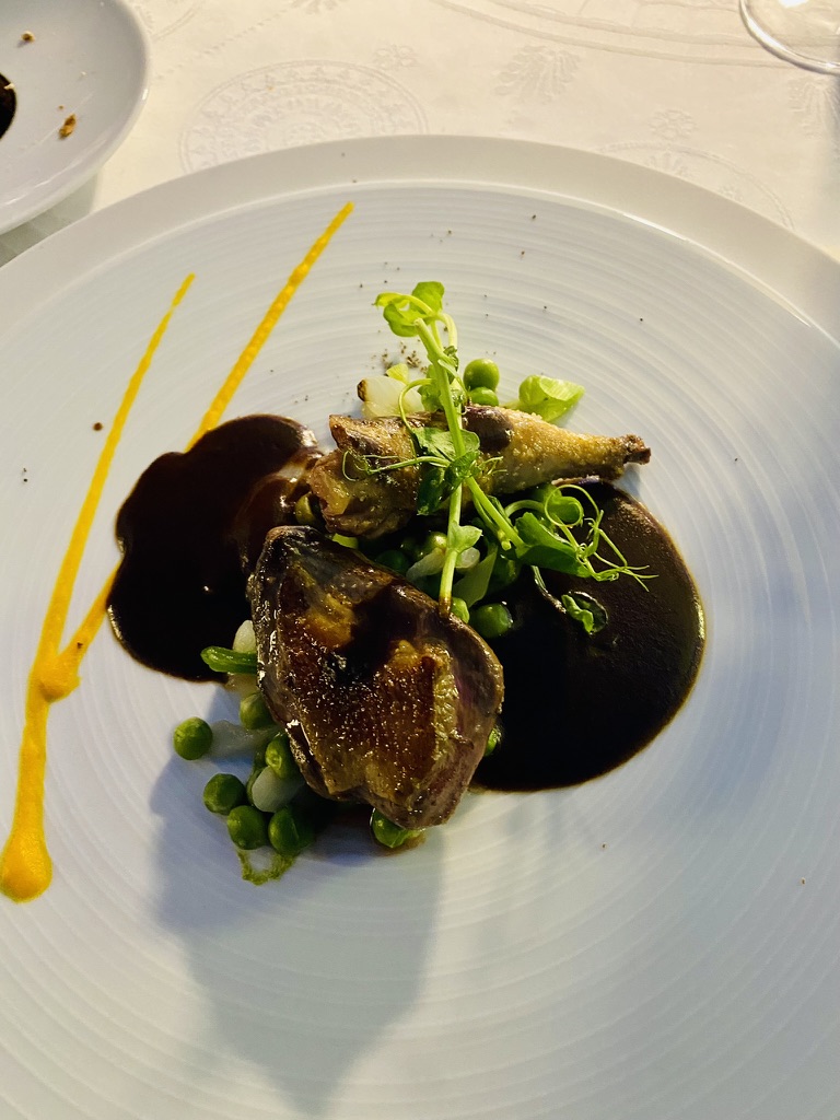 A roasted quail plate at Le Vieux Logis, with peas, pearl onions, pea shoots, glossy reduction sauce, and two parallel turmeric brushstrokes.