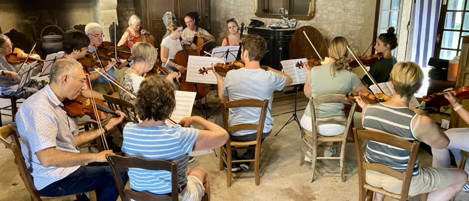 A chamber music ensemble in the grange at the estate — violins, cellos, music stands, fireplace and gilt mirror in the background.