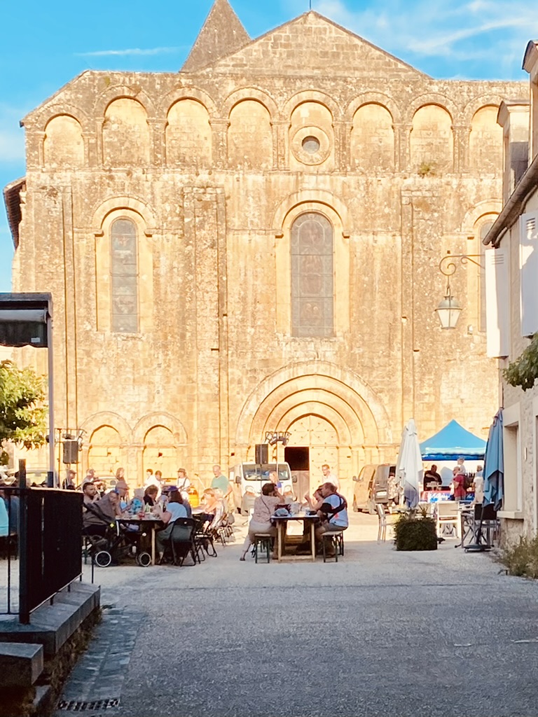 The Romanesque facade of the Cadouin abbey at golden hour, with the Wednesday market and trestle tables on the cobbled square below