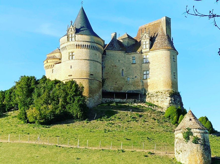 Château de Bannes at golden hour, perched on its hilltop with a small stone pigeonnier on its own knoll in the foreground