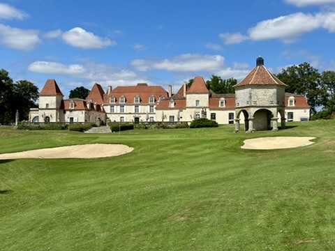 The Château des Vigiers seen from the 18th green — pepperpot turrets, the round dovecote, fairway and bunkers in the foreground, late summer sky