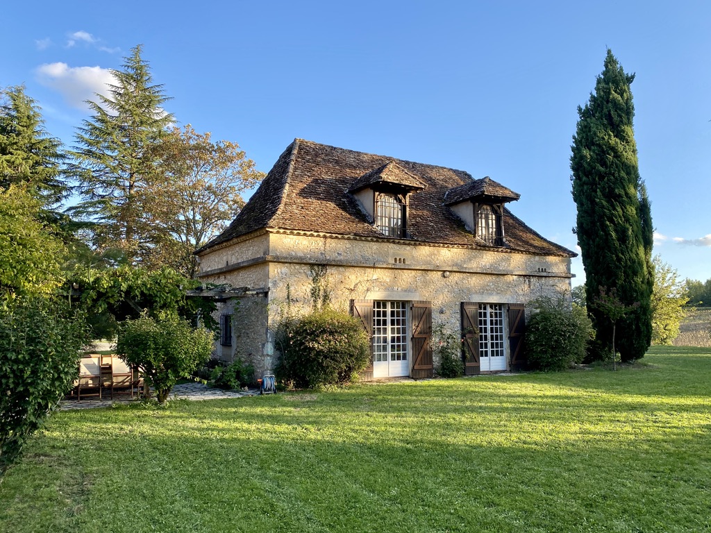 Jardin — the pretty stone house in the courtyard — at golden hour, with the cypress, the cedar, and the lawn sloping down to it