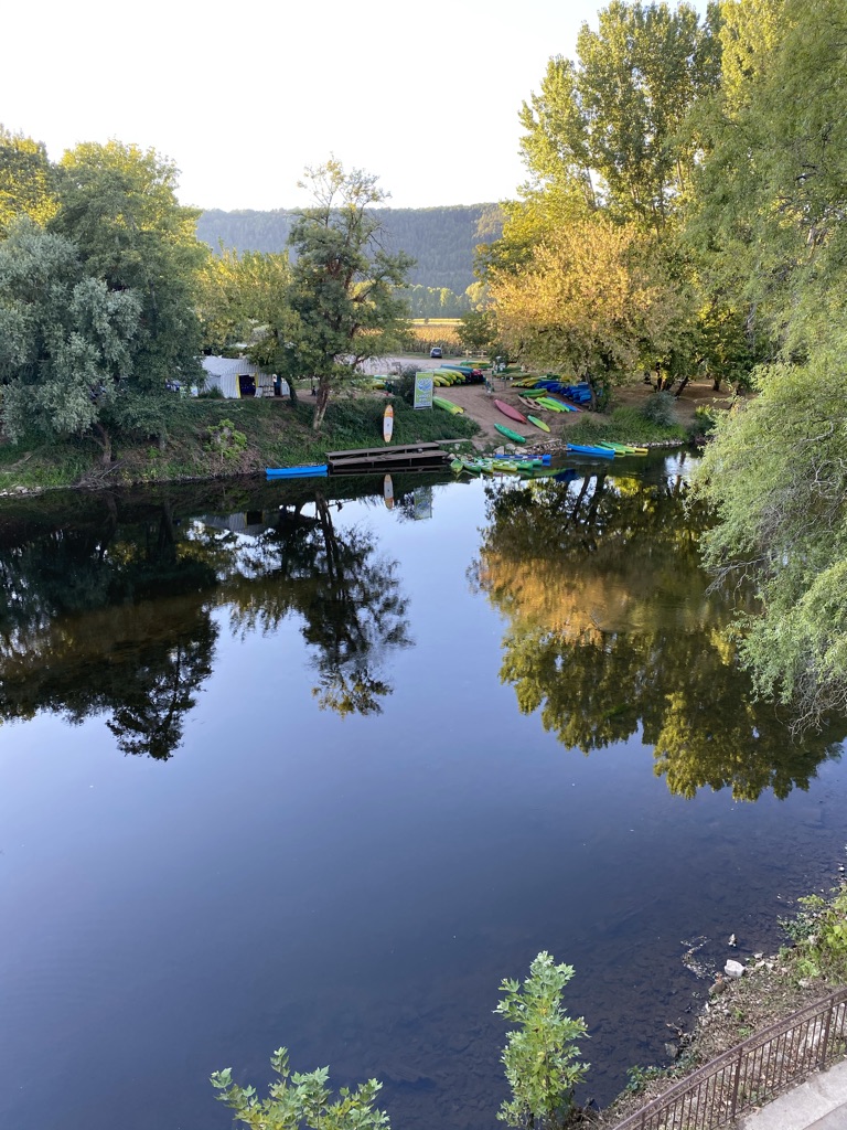 A line of kayaks and stand-up paddleboards at a launch dock on the Vézère, the river still and reflecting trees in golden light