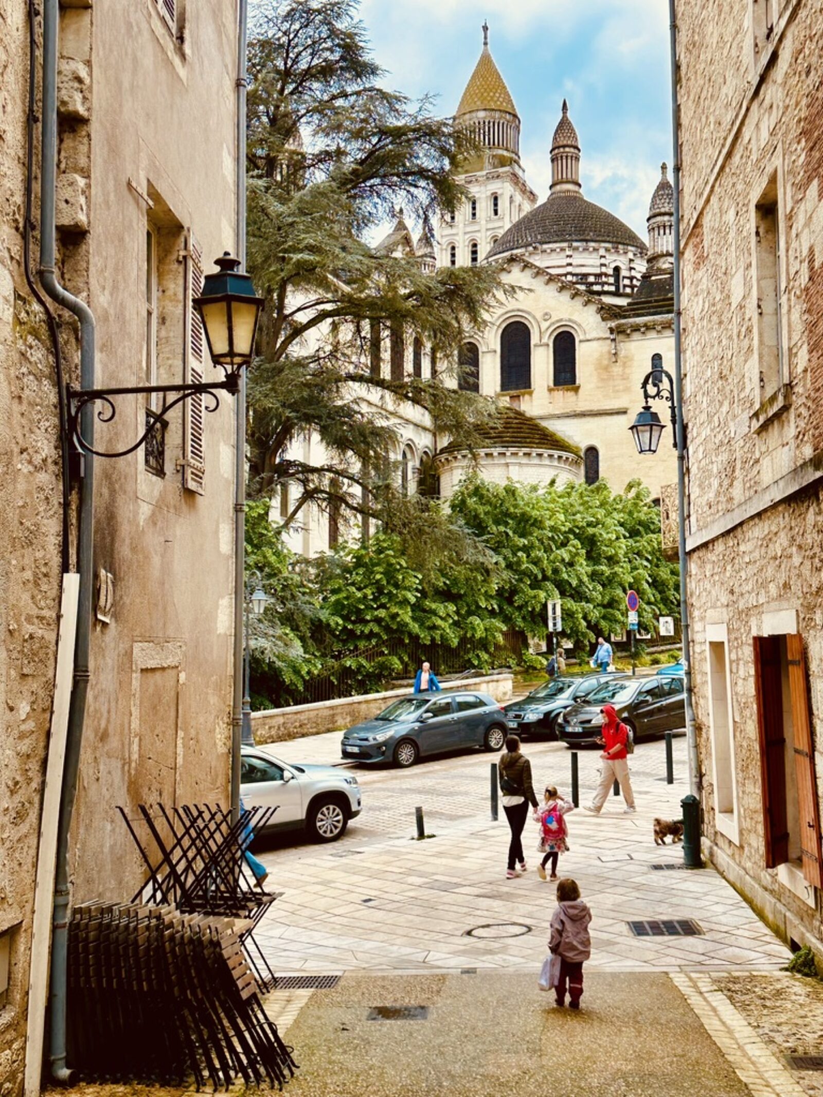 The domes of Saint-Front cathedral in Périgueux rising above the old town — Romano-Byzantine style with stone conical roofs and gilded details, seen through a gap between two ochre-coloured old buildings, cedar tree in the foreground