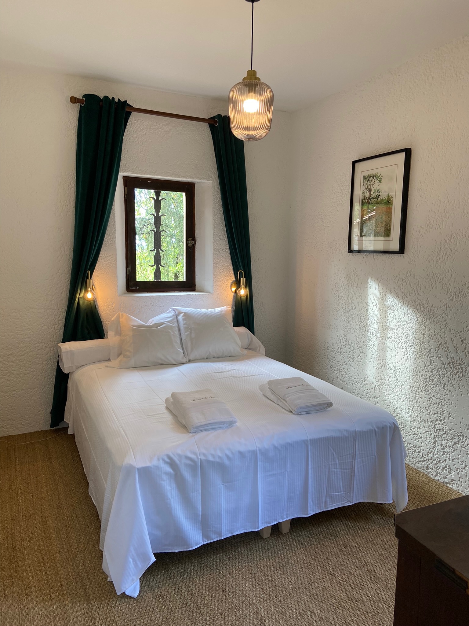 Bedroom one at Le Pigeonnier, with a deep-set iron-grilled window, dark green velvet curtains and brass wall lights