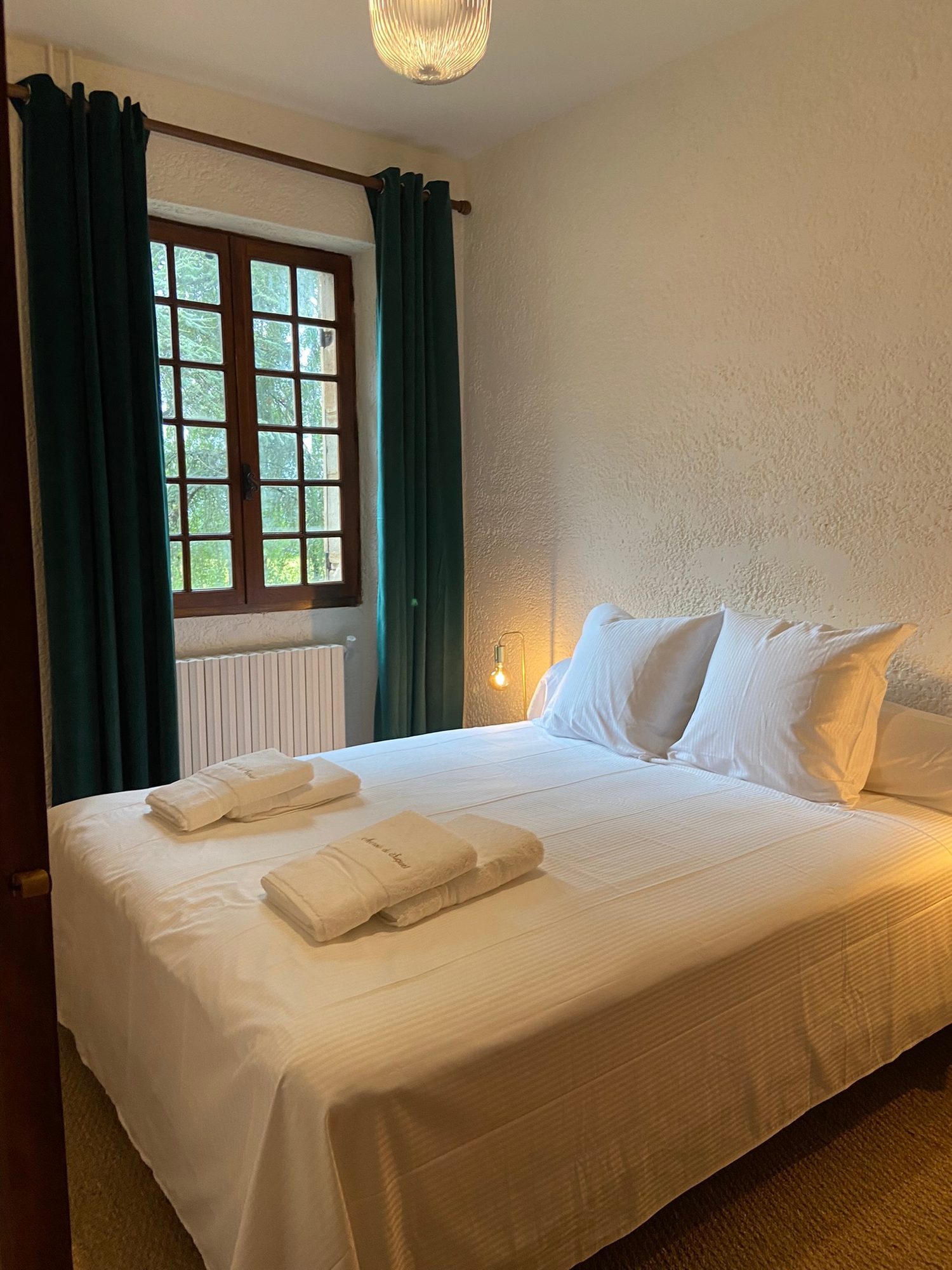 Deuxième chambre du Pigeonnier, haute croisée en bois sombre, rideaux de velours vert et radiateur en dessous