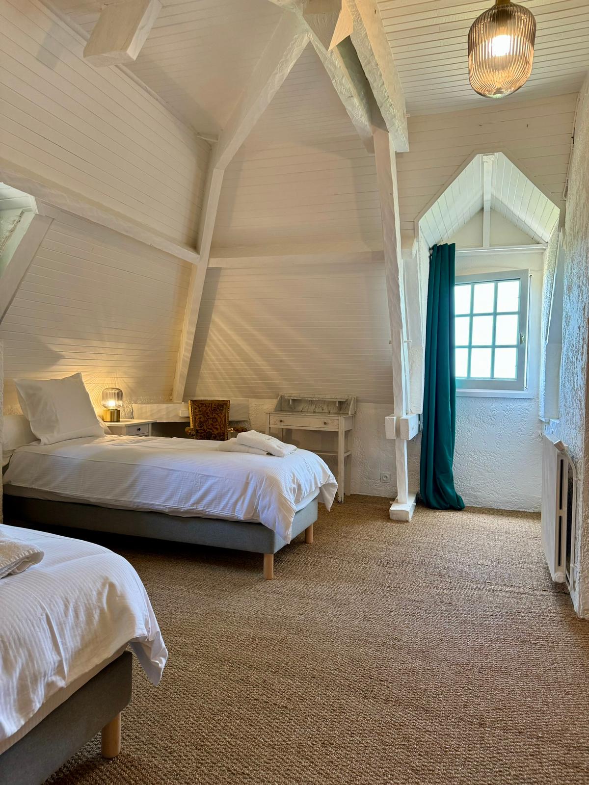 Bedroom three at Le Pigeonnier, under whitewashed roof timbers with two single beds either side of a dormer window