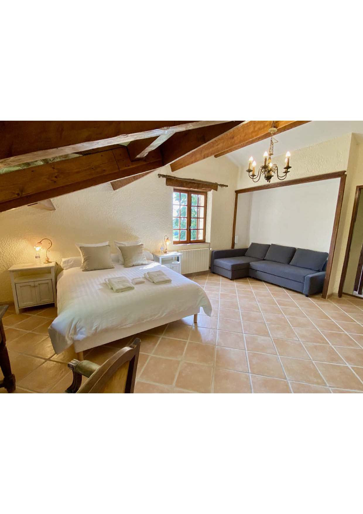 The family room at Maison des Tournesols, with a double bed and corner sofa bed under the roof timbers