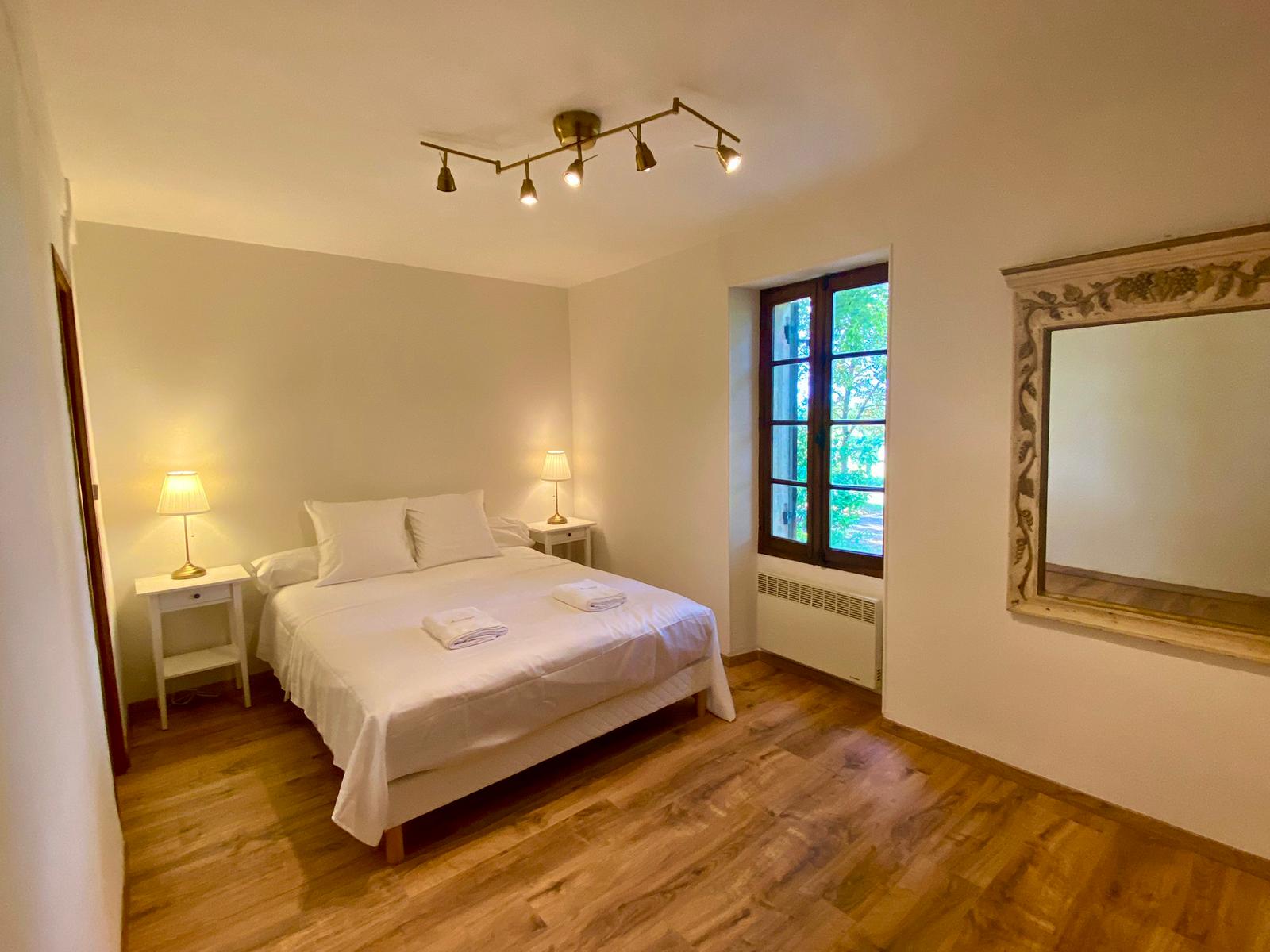 The ground-floor bedroom at Maison des Vignes, with a carved stone mirror and tall window