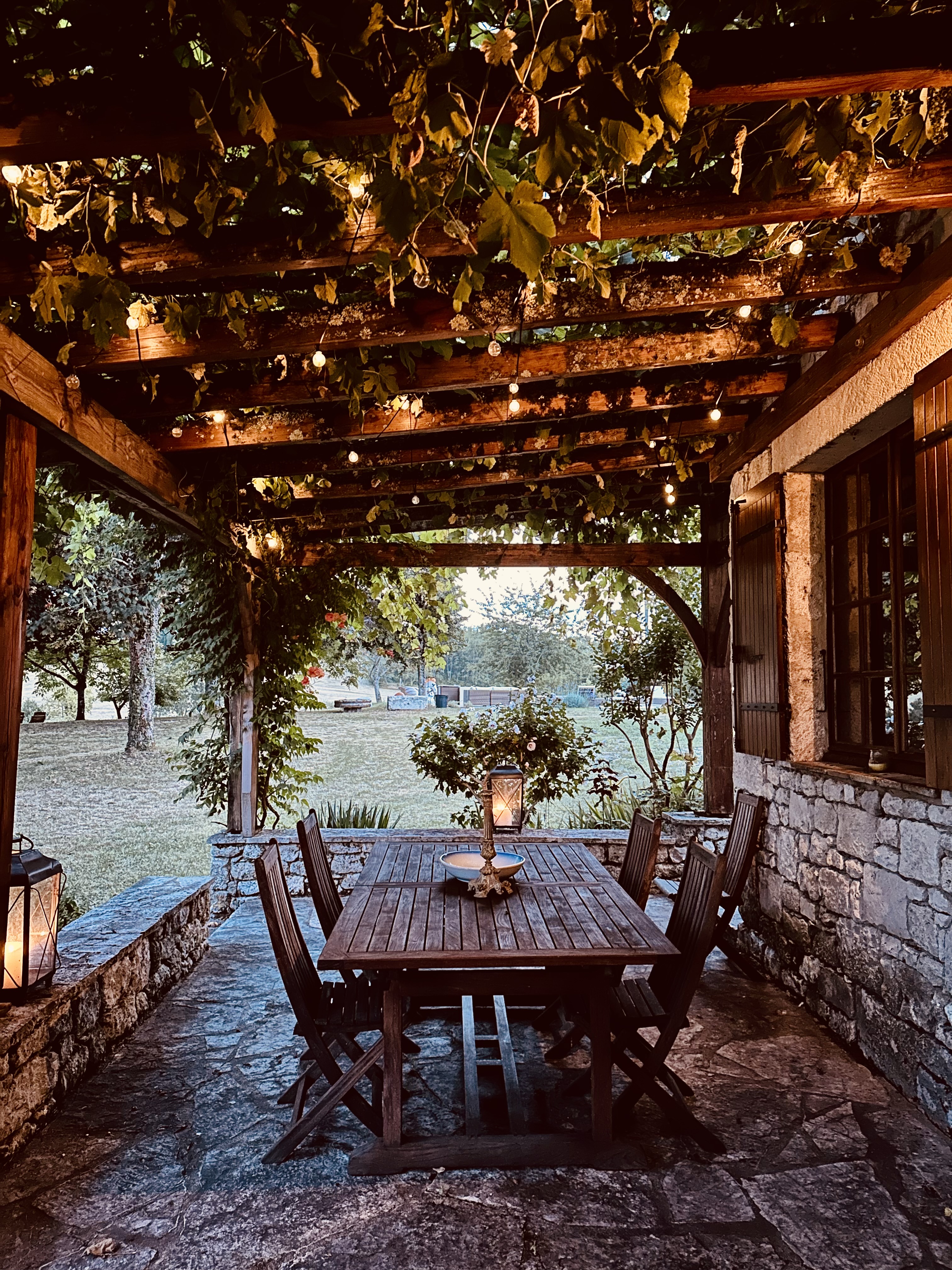 The vine-covered porch at Maison des Vignes at dusk, lit with string lights and lanterns