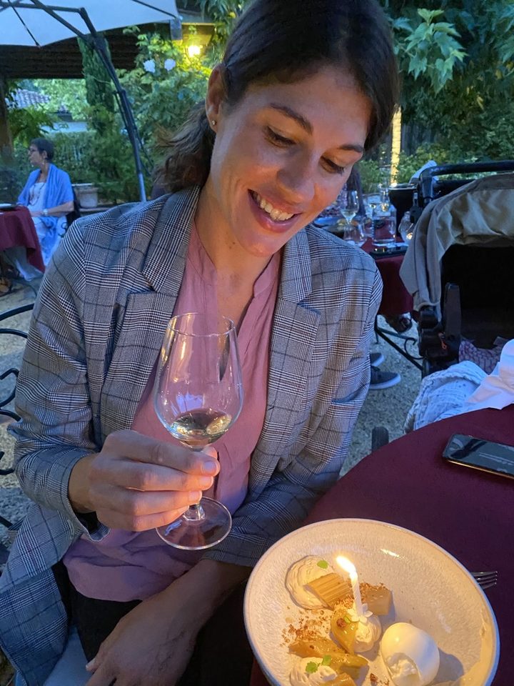 Stéphanie laughing at the table, holding a glass of white wine, a candle lit on a dessert in front of her — the kind of moment the article describes.